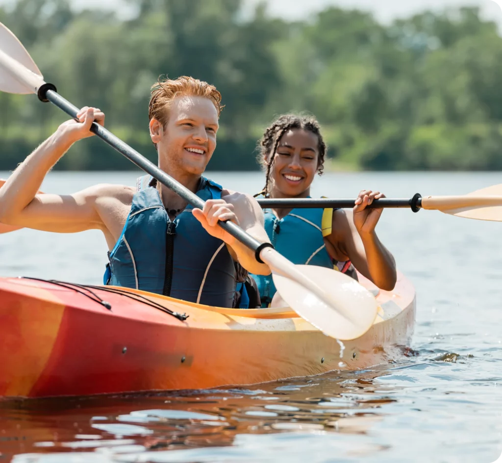 Two people wearing life jackets paddle together in a tandem kayak on a calm lake, surrounded by trees on a sunny day—perfect for those seeking scenic kayak tours.